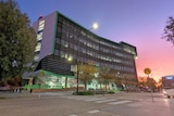 A large office block with green letters spelling out 'HUME' is under a pink and blue sky.