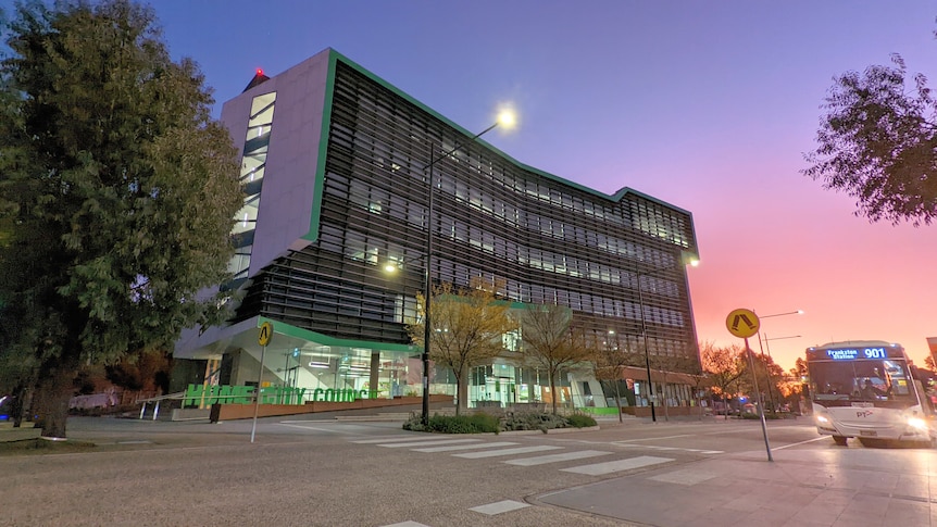 A large office block with green letters spelling out 'HUME' is under a pink and blue sky.