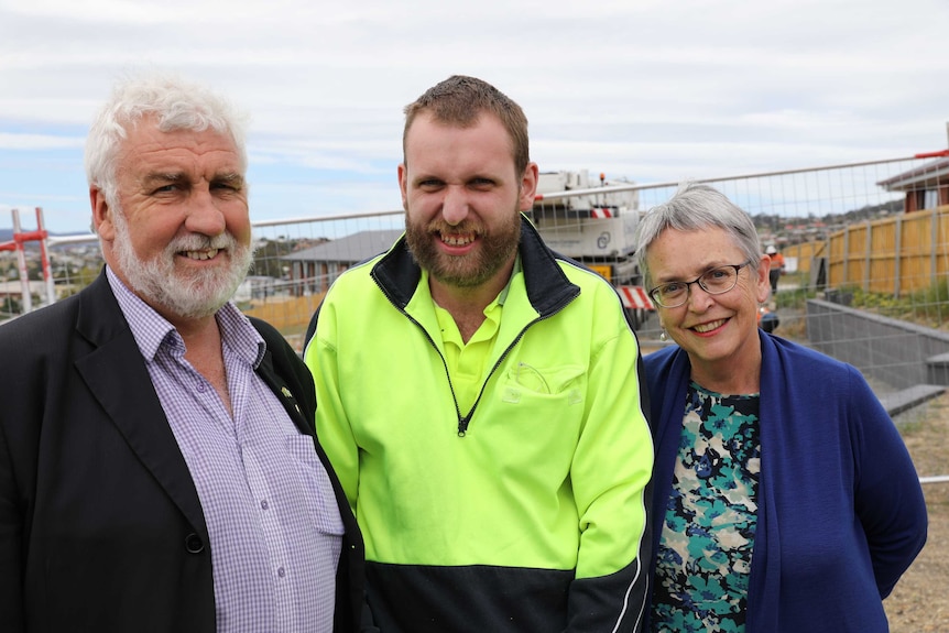 Bob Gordon, Jack Gordon and Dianne Snowden stand in front of a fence at the Supported Affordable Accommodation site at Glenorchy