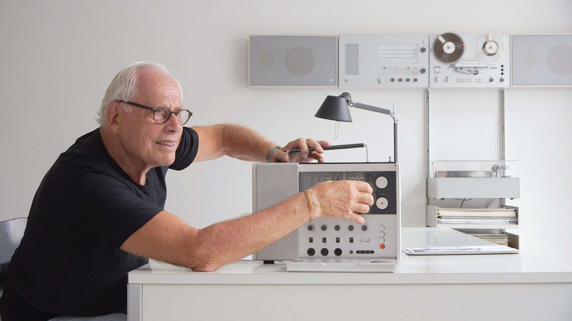 A man with white hair and glasses operates a radio.