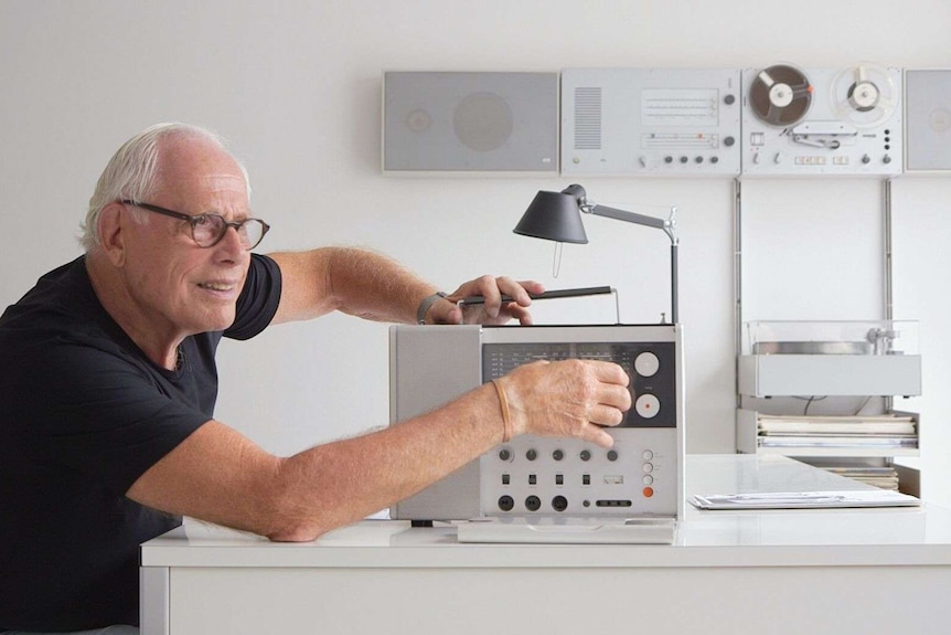 A man with white hair and glasses operates a radio.