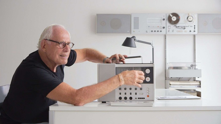 A man with white hair and glasses operates a radio.