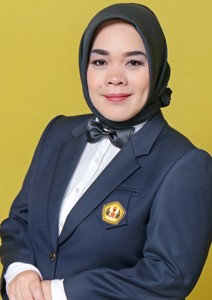 A woman, wearing dark grey suit and hijab smiling, looking at the camera.