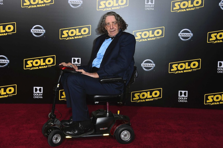 An actor in a mobility wheelchair looks at the media at a film premiere's red carpet