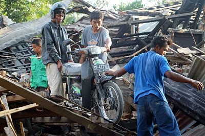 An Indonesia youth carries his motorbike through the ruins of a house near Yogyakarta