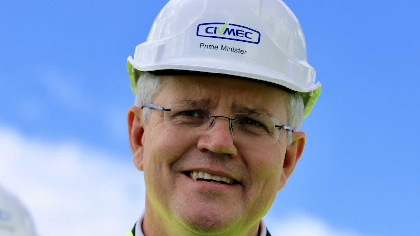 Prime Minister Scott Morrison in close-up and smiling and wearing a hard hat against a blue sky.