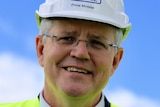 Prime Minister Scott Morrison in close-up and smiling and wearing a hard hat against a blue sky.
