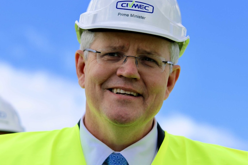 Prime Minister Scott Morrison in close-up and smiling and wearing a hard hat against a blue sky.