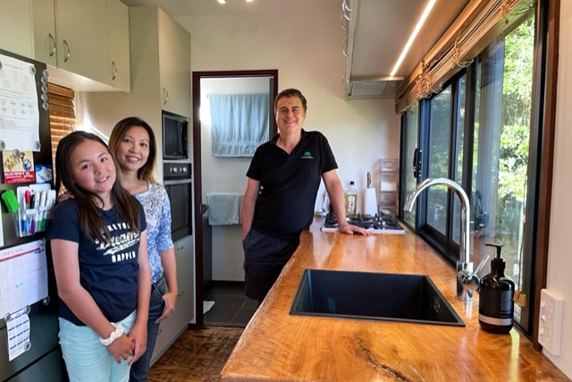 Peter standing in his tiny home's kitchen with his wife and daughter. 