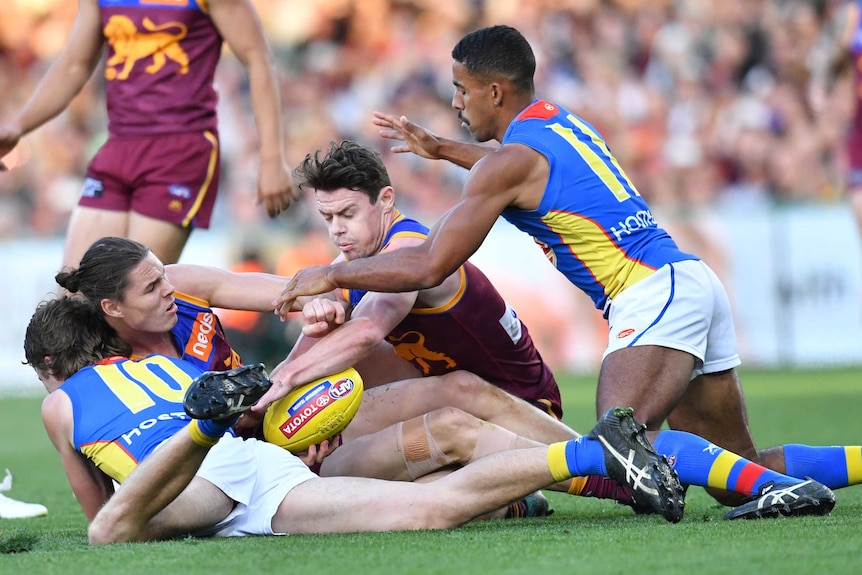 Brisbane Lions and Gold Coast Suns AFL players contest the ball on the ground.