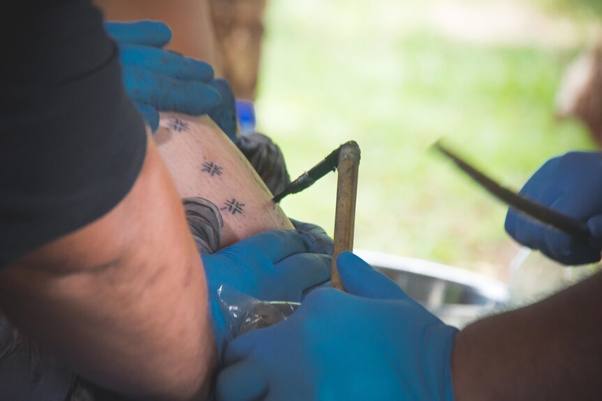 Hands wearing gloves stretch the skin as a master tatooist holds the 'au about to tap.