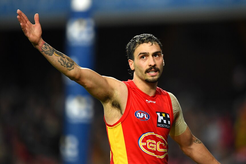 A Gold Coast AFL player raises his arm in salute to the crowd after his goal during a game.