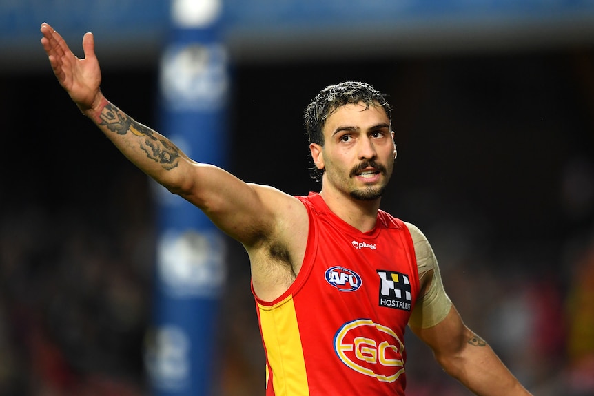 A Gold Coast AFL player raises his arm in salute to the crowd after his goal during a game.