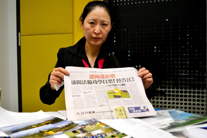 Woman holding a newspaper behind a table full of paperwork