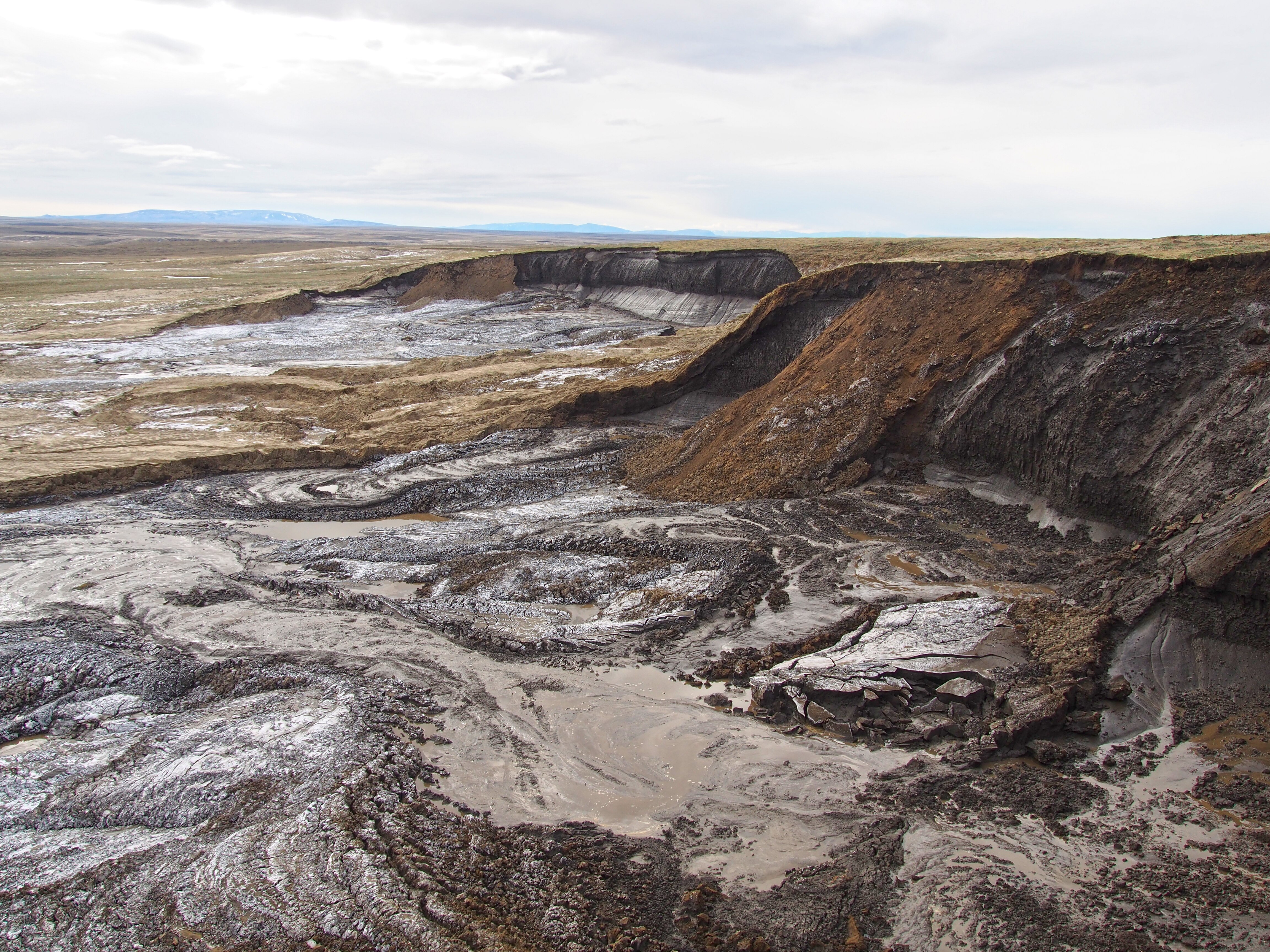 A muddy landscape where white flecks are sparse showing an area where permafrost has melted.
