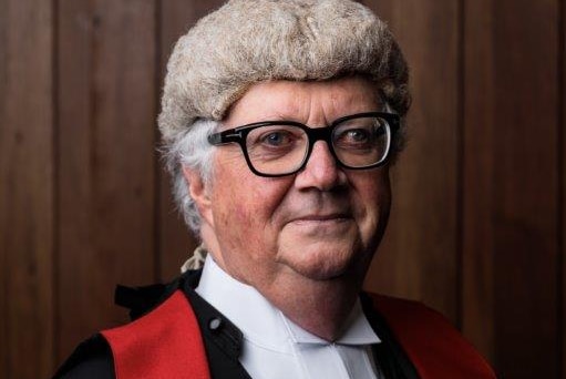 Chief Justice Alan Blow wearing a wig and judge's robes in front of a wood-panelled wall