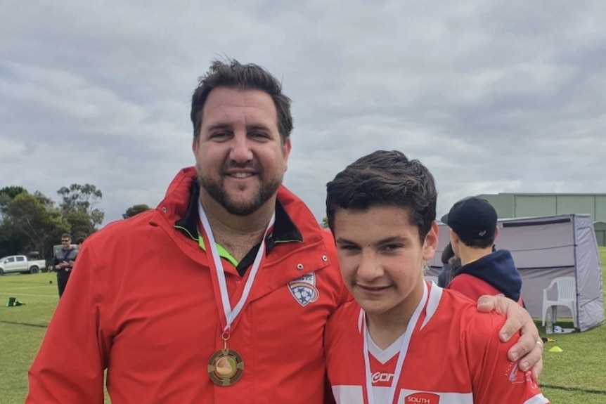 A father and son celebrate a winning medal in a soccer carnival wearing red.