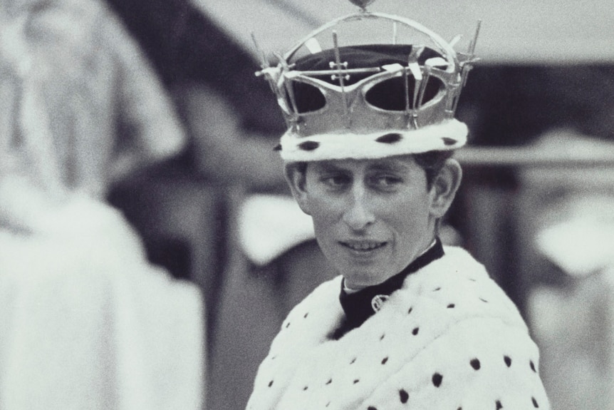 A young Prince Charles wearing a crown and white fur robe with black spots.