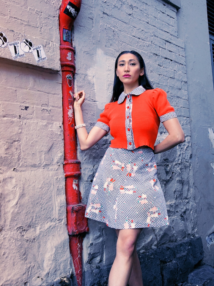 A young woman with long black hair wearing a red and blue two piece in a laneway