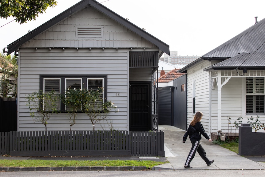 Someone walks past a Melbourne weatherboard house on a suburban street.