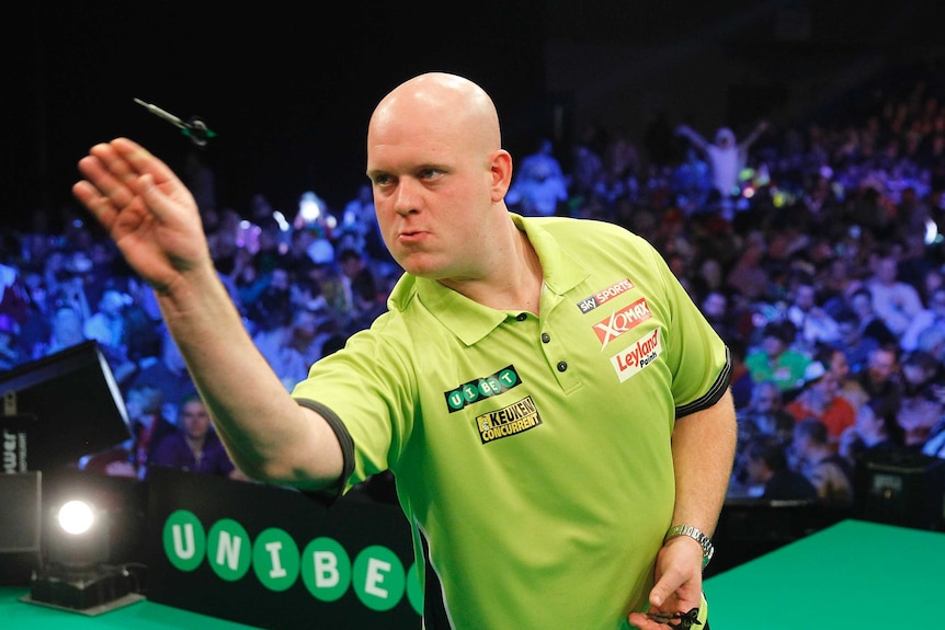 A darts player throws a dart with fans jumping up and down in the background