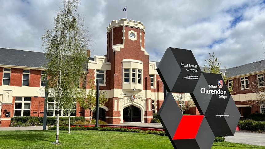 Exterior of ballarat clarendon college with sign , cream and red Victorian building, has a flag on top.