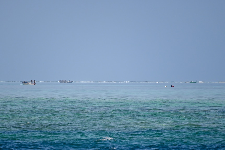 Tiga perahu dan dua orang berenang di air di cakrawala.