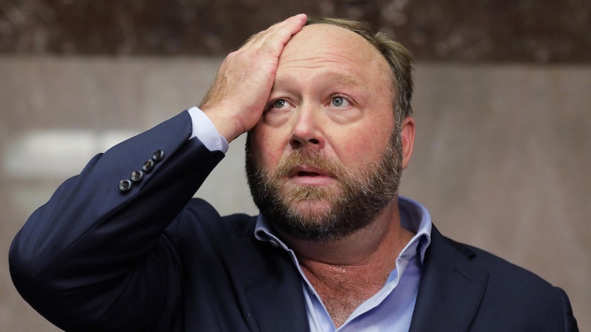Alex Jones wipes his brow as he speaks to the media out a Senator's office during a hearing in Washington, 2018.