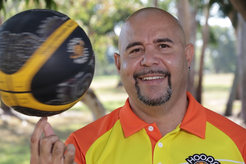 A man with a goatee spins a basketball on his finger