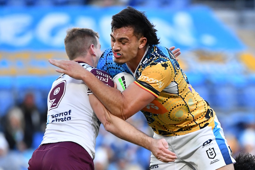 A Gold Coast Titans NRL player is tackled around his upper body by a Manly opponent.