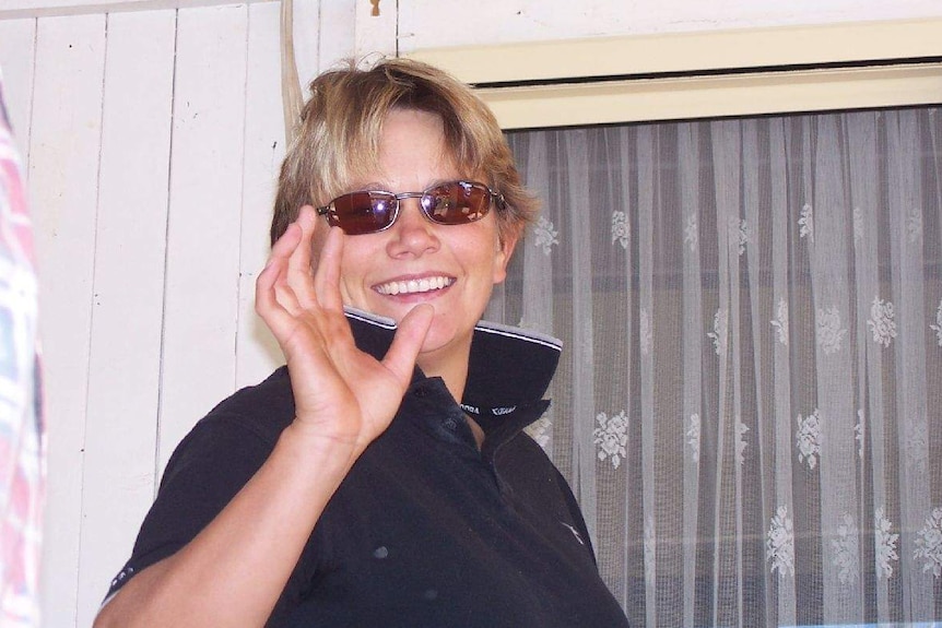 Lainie Coldwell smiles and waves at the camera wearing a polo shirt and sunglasses.