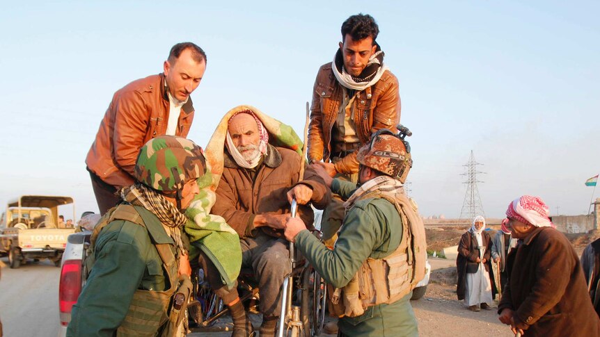 Kurdish security forces help an elderly man from the minority Yazidi sect