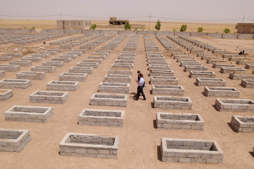 Aerial shot of coffin-shaped holes in a grid pattern and two people walking down the centre