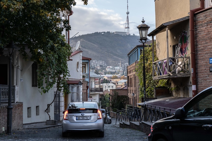Cars drive on a cobblestone street overlooking the old town of Tsibli