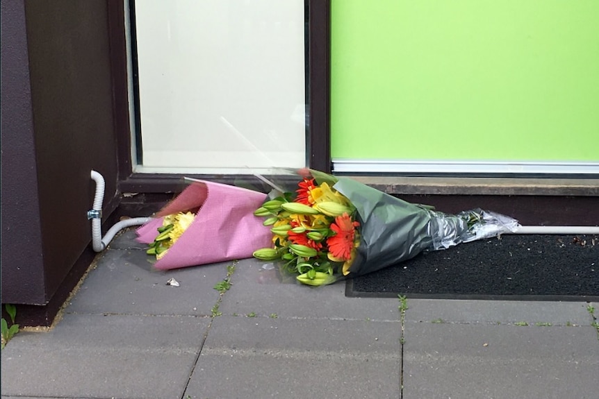 Two bunches of flowers sit on a doormat.