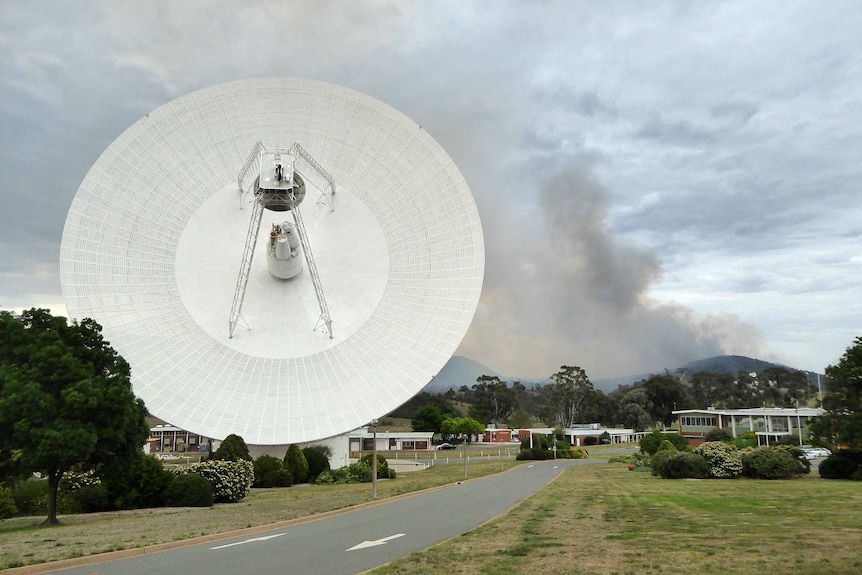 Smoke rises from the hills behind a huge satellite dish.