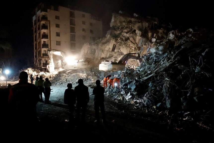people wait nearby as emergency workers search through rubble of an earthquake in Antakya