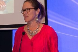 A bespectacled woman with dark hair speaks at a podium.