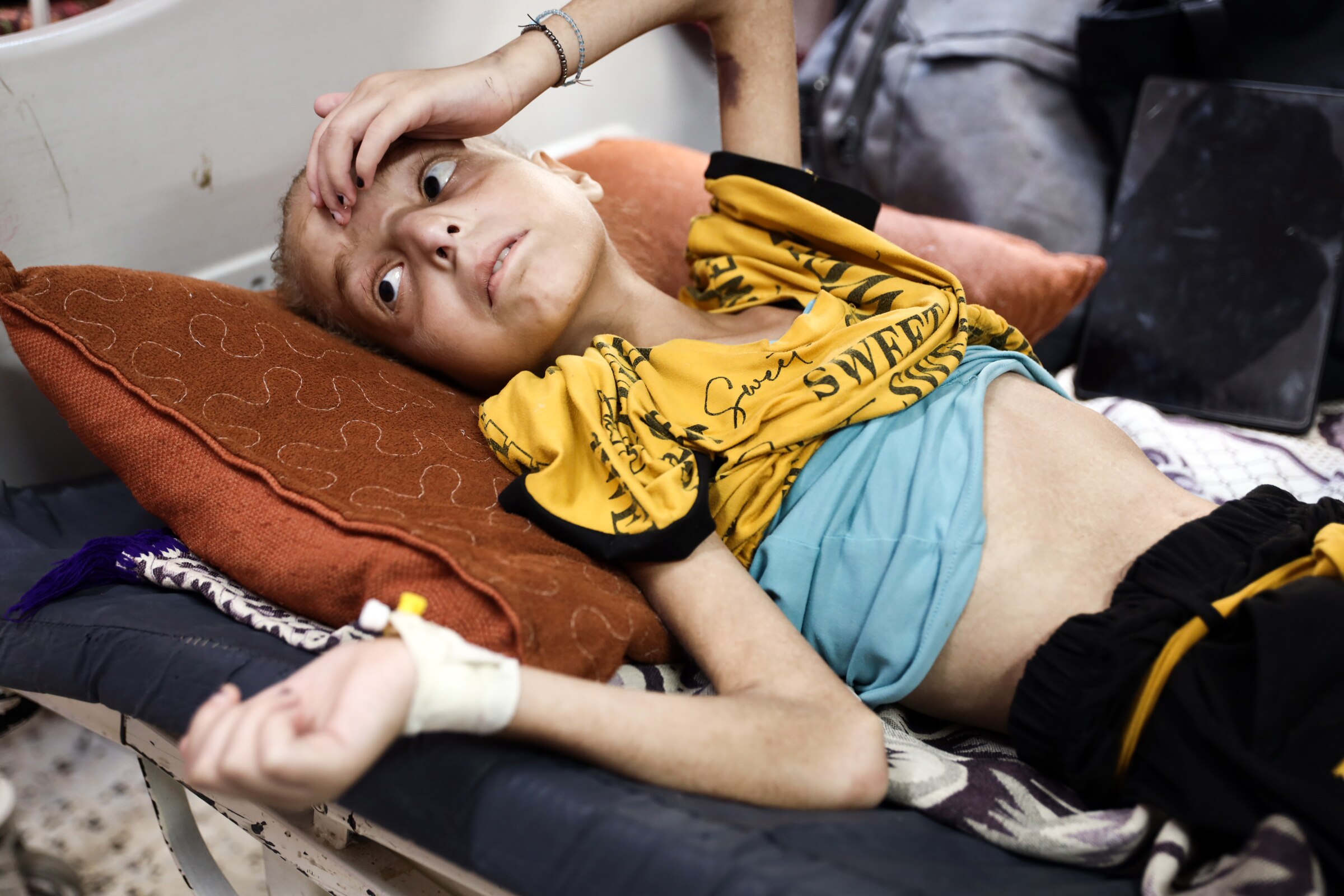A 12-year-old girl lies on a hospital bed, with a bandage around one wrist and her hand on her forehead.