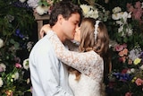 Bindi Irwin and Chandler Powell, in wedding dress and suit, embrace and kiss at their wedding ceremony.