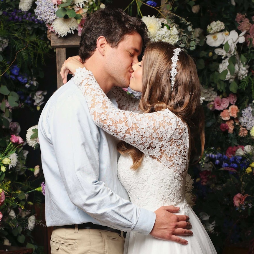 Bindi Irwin and Chandler Powell, in wedding dress and suit, embrace and kiss at their wedding ceremony.