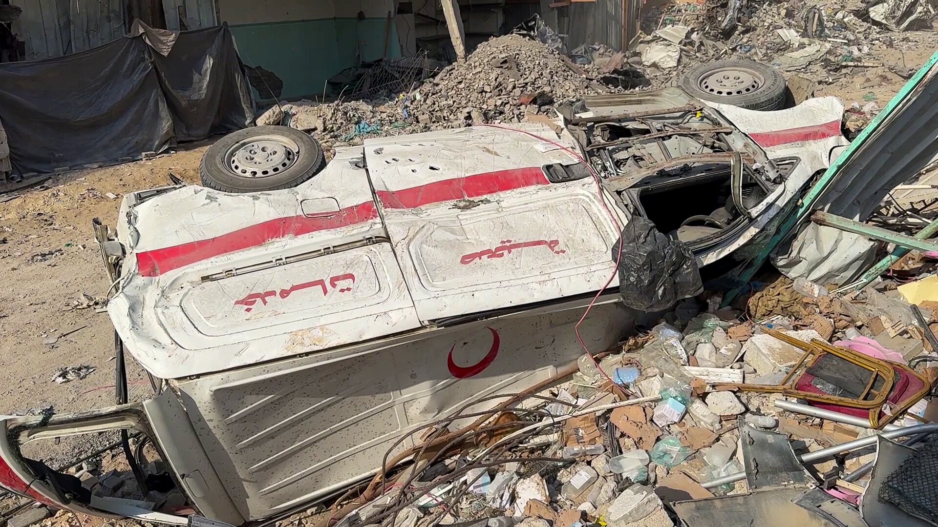 A destroyed ambulance lies on its side near the wreckage of a building outside Kamal Adwan hospital.