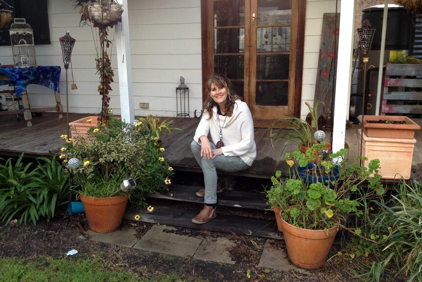 Jenny sits on a wooden verandah, surrounded by flower-filled pots.