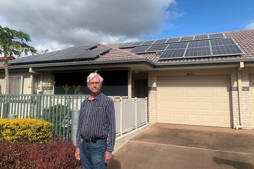 A man stands in front of a house with solar panels on the roof.
