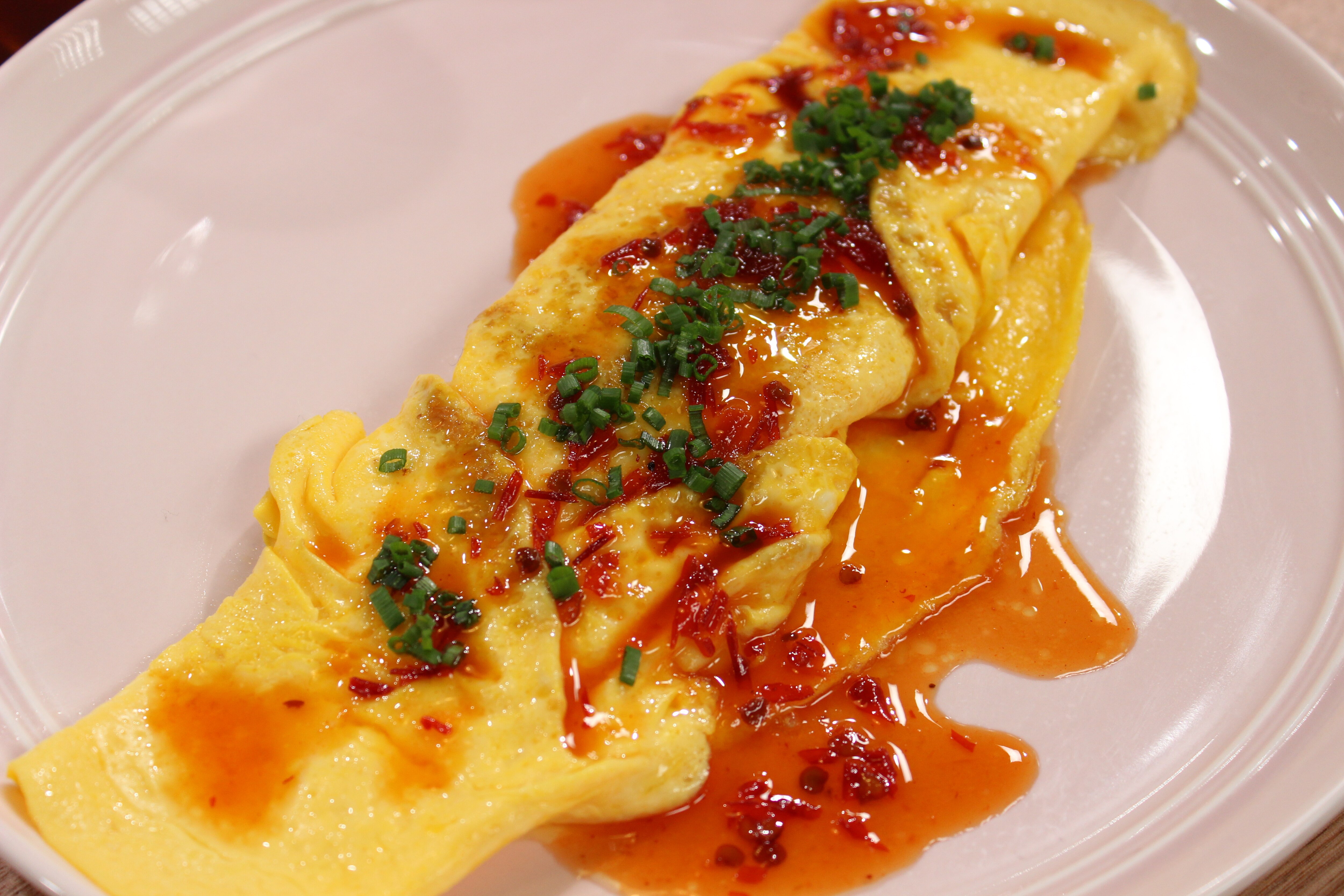 A picture of a finished dish of a classic egg omelette with cheese, chilli oil and herbs.