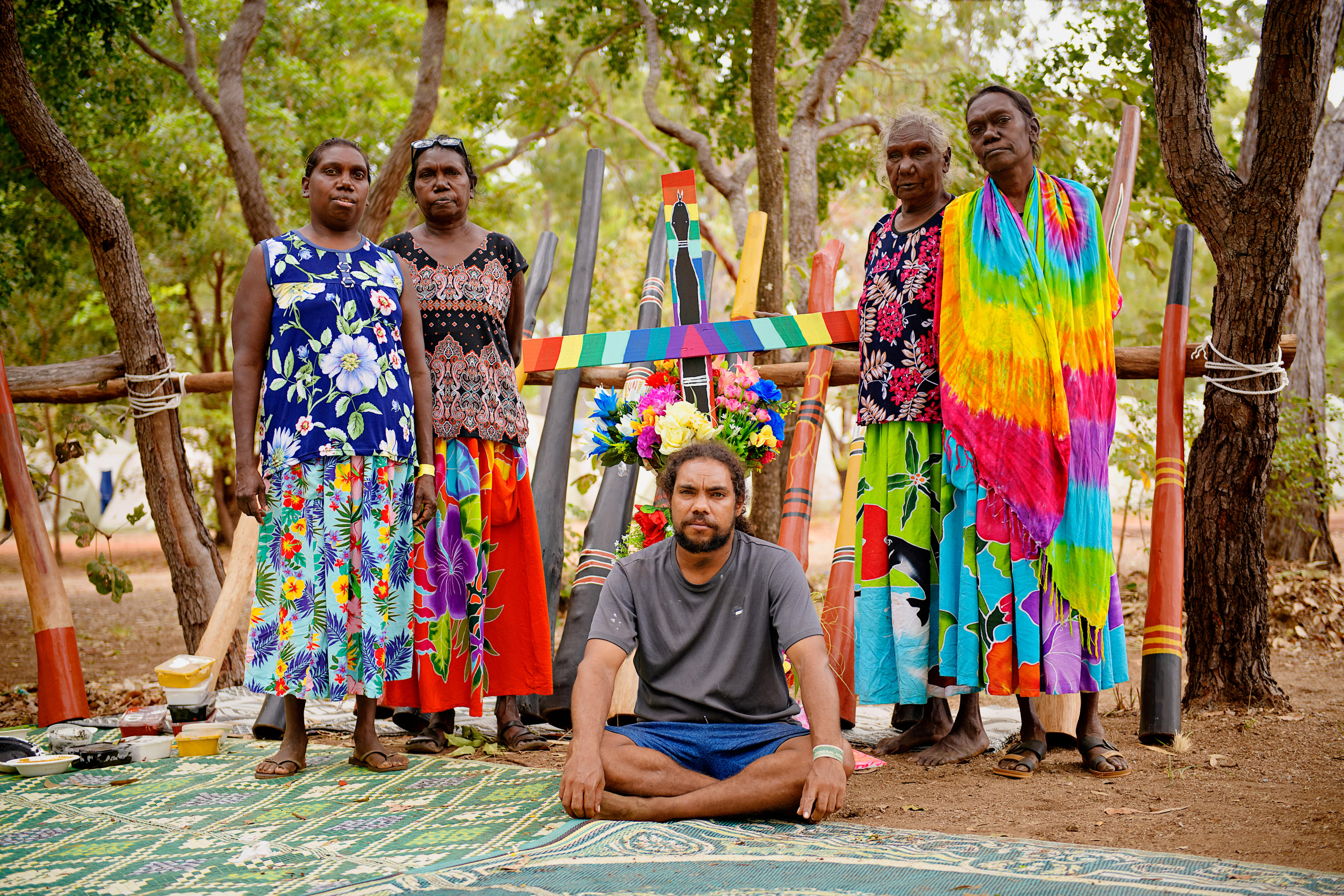 Four women standing and a man sitting in front of colorful Yidak didgeridoo. 