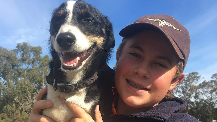 A teenager in a baseball cap and navy jumper holds up a dog.