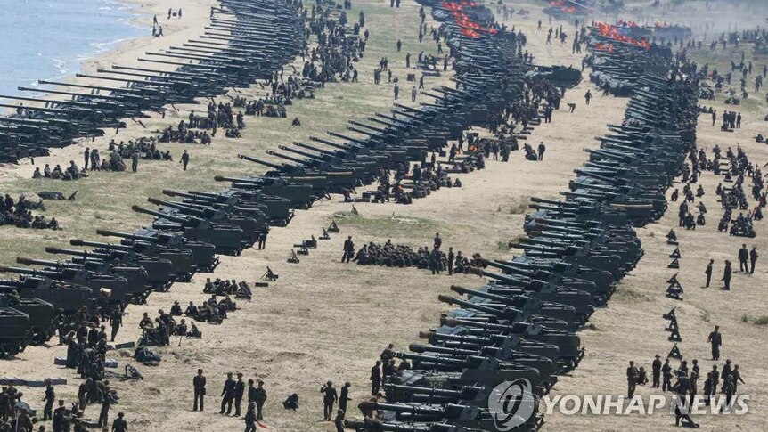 Lines of soldiers with large weapons fill a beach in North Korea.