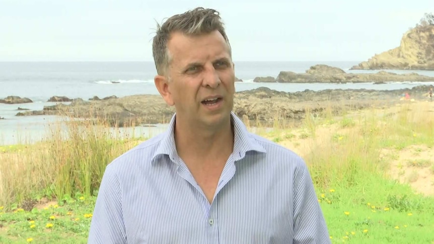 a man in a collared shirt standing by a rocky beach