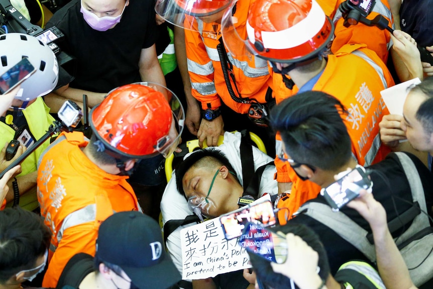 A man on a stretcher with his eyes closed surrounded by medics in orange vests and helmets